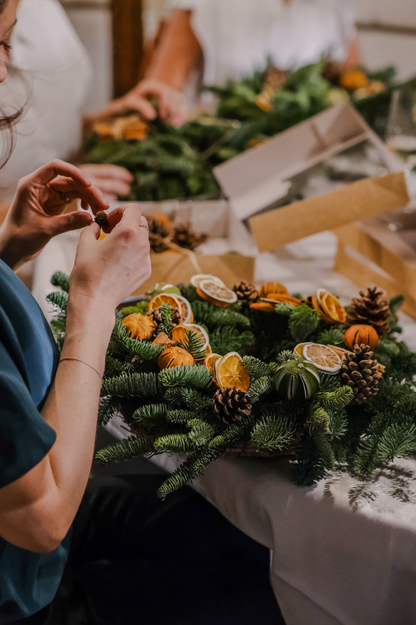 Guest decorating a 100% natural Christmas wreath with dried orange slices and pine cones at the workshop
